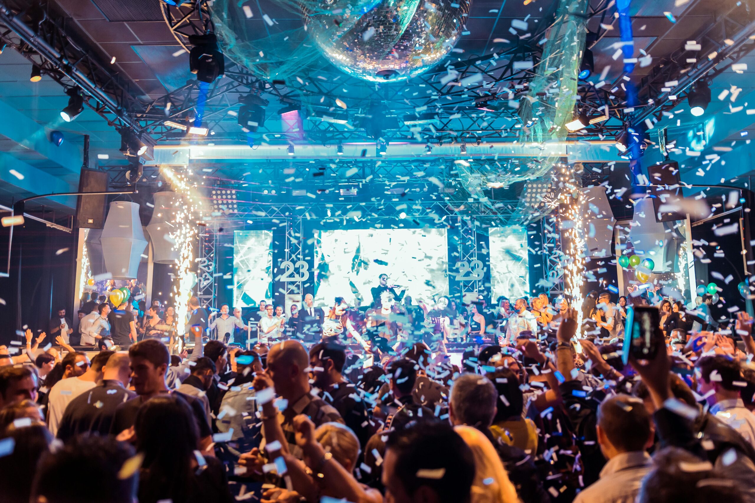 Vibrant nightclub scene in Mantua, Italy, featuring a lively crowd, confetti, and colorful lights.